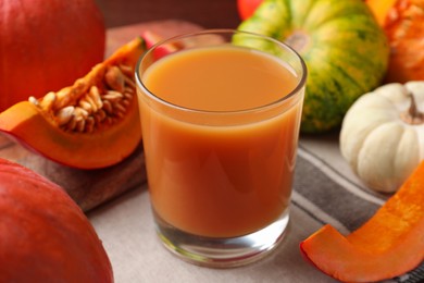 Photo of Tasty pumpkin juice in glass and different pumpkins on table