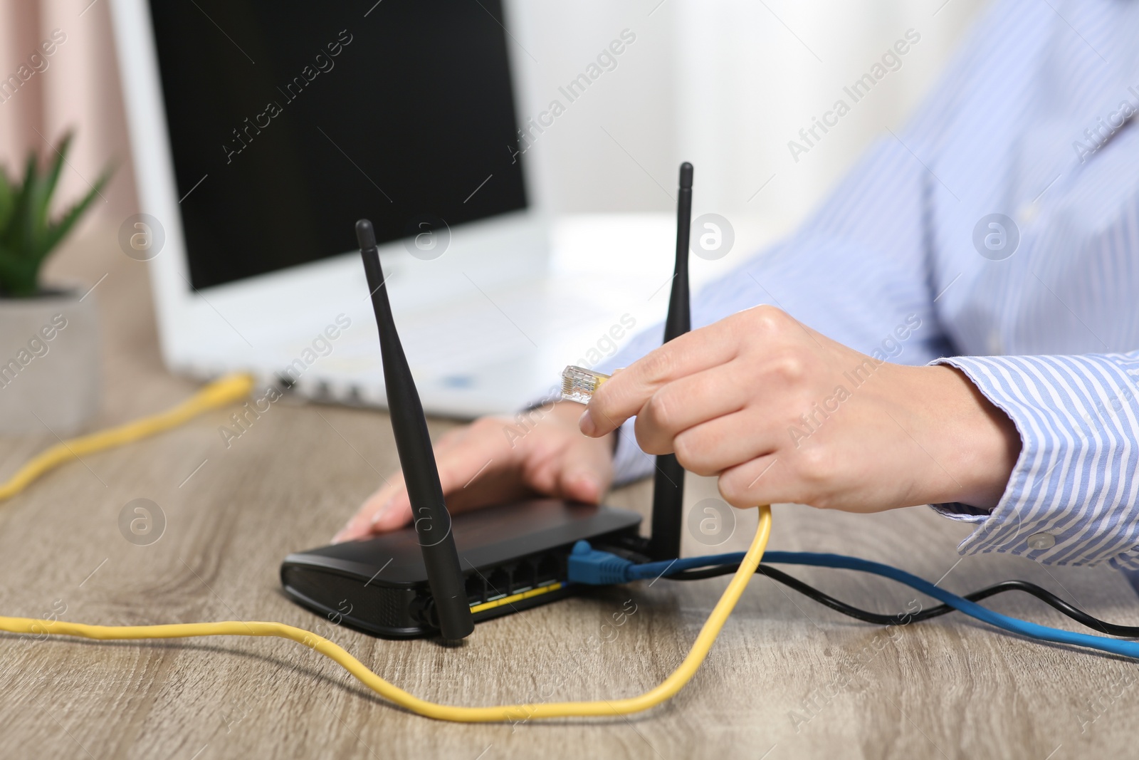 Photo of Woman inserting ethernet cable into Wi-Fi router at wooden table indoors, closeup