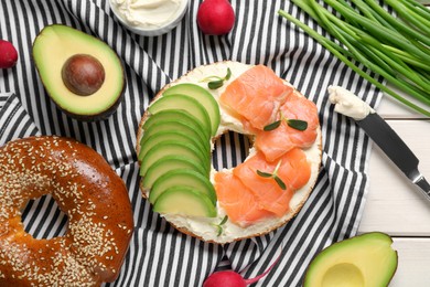 Photo of Delicious bagel with cream cheese, salmon and avocado on table, flat lay