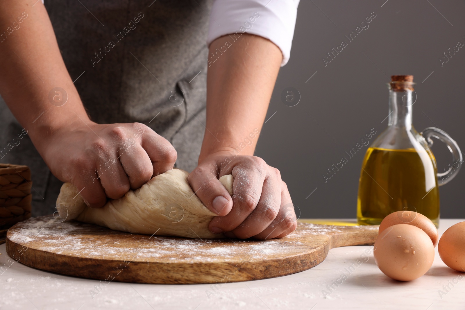 Photo of Man kneading dough at table near grey wall, closeup