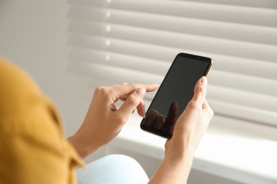 Photo of Young woman using modern smartphone indoors, closeup