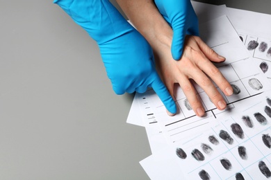 Photo of Investigator taking fingerprints of suspect on grey table, closeup. Space for text