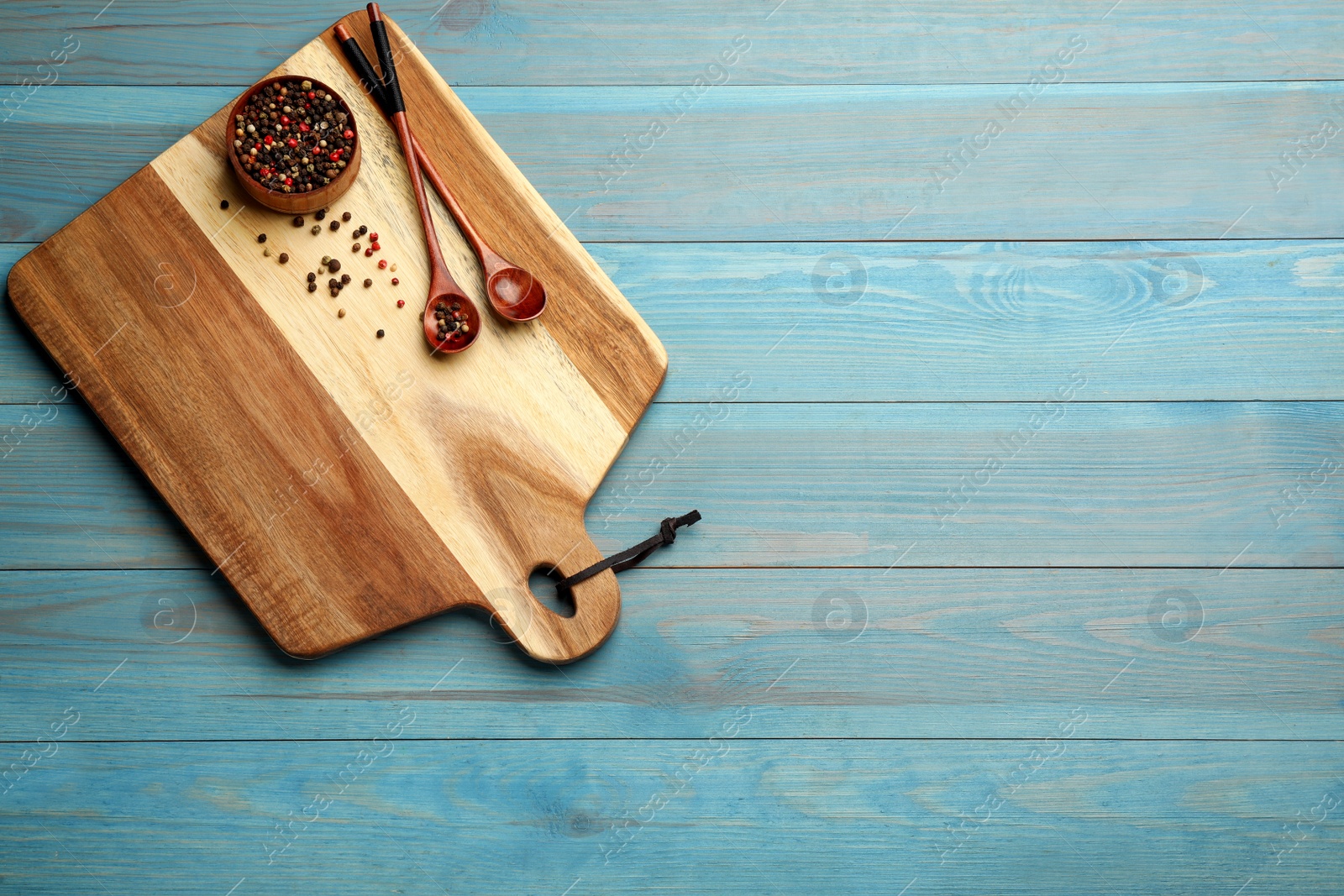 Photo of Cutting board, peppercorn and spoons on blue wooden table, top view with space for text. Cooking utensils