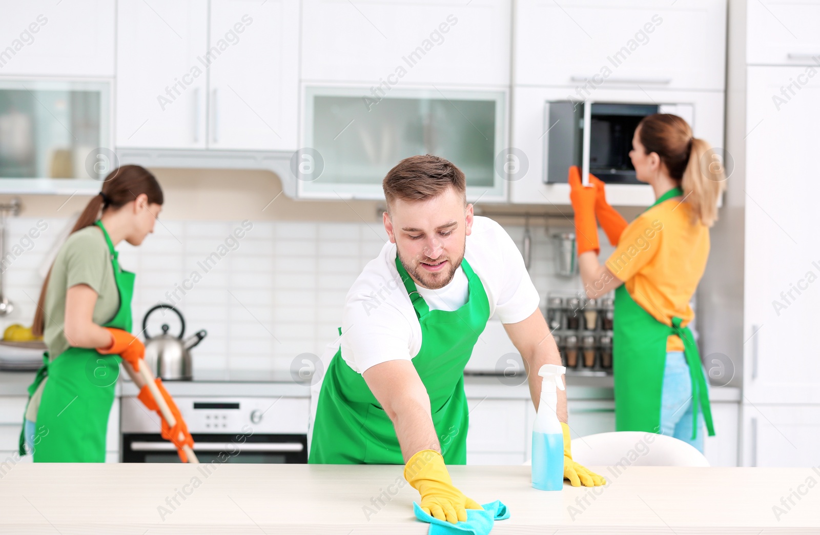 Photo of Team of professional janitors in uniform cleaning kitchen