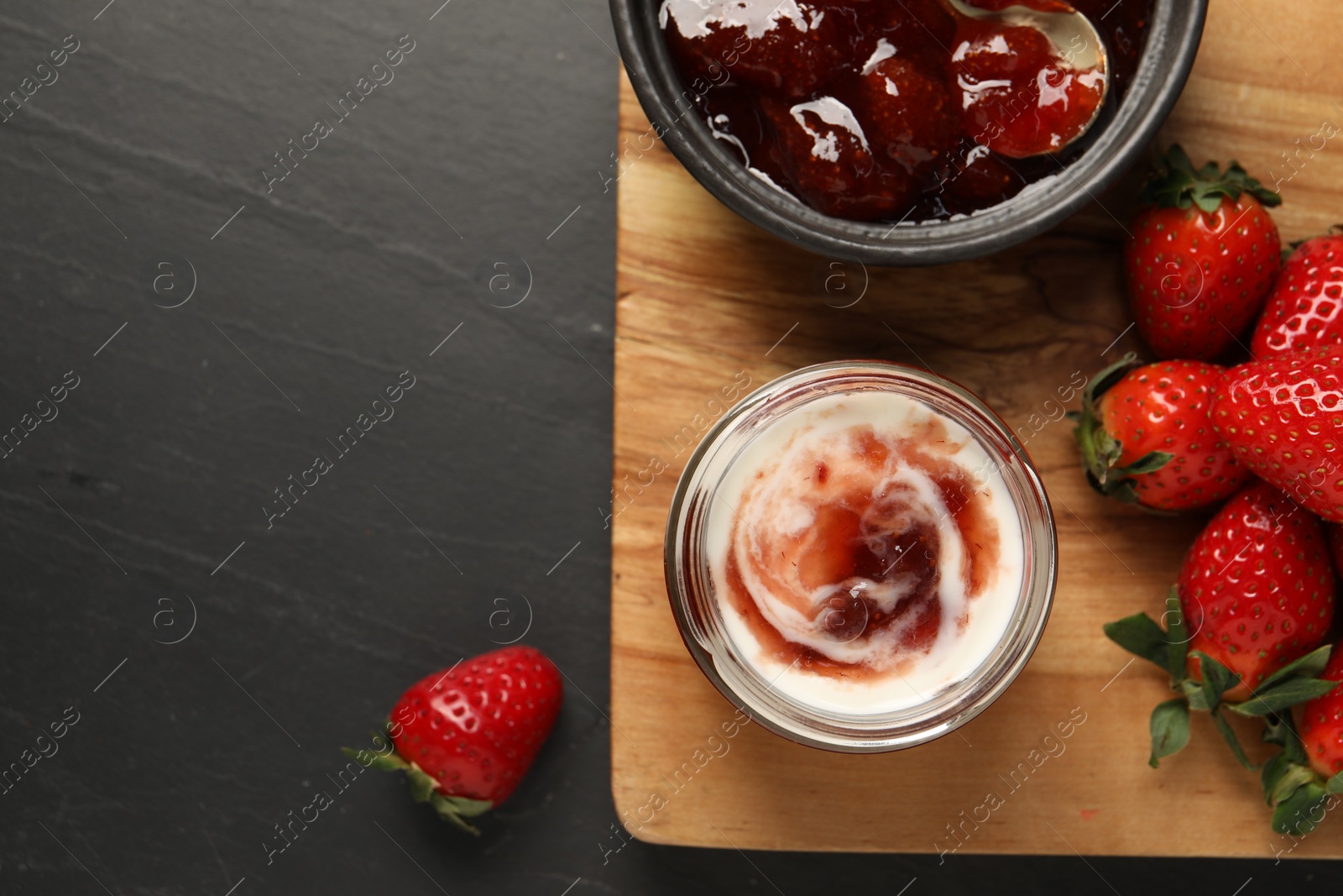 Photo of Tasty yoghurt with jam and strawberries on black table, top view. Space for text