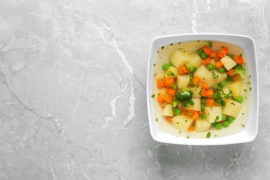 Photo of Bowl of fresh homemade vegetable soup on grey marble background, top view. Space for text