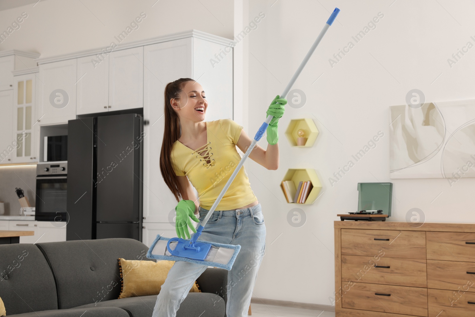 Photo of Spring cleaning. Young woman with mop singing while tidying up at home