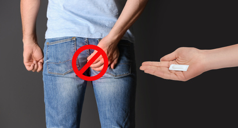 Woman holding suppository for hemorrhoid treatment and man suffering from pain on black background, closeup