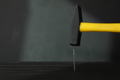 Photo of Hammering metal nail on wooden table against black background. Space for text