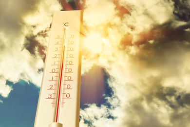 Image of Weather thermometer showing high temperature and sunny sky with clouds on background