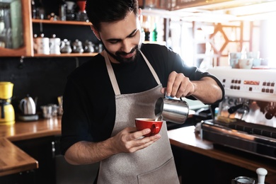 Photo of Barista pouring milk into cup of coffee in shop