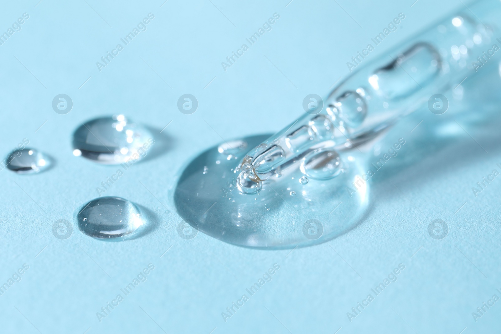 Photo of Glass pipette and transparent liquid on light blue background, closeup