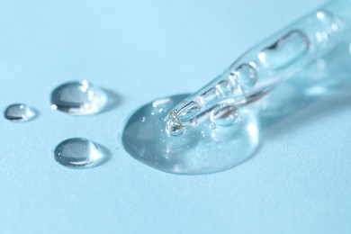 Photo of Glass pipette and transparent liquid on light blue background, closeup