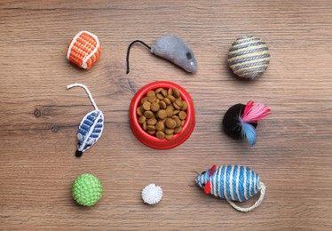 Different pet toys and feeding bowl on wooden background, flat lay