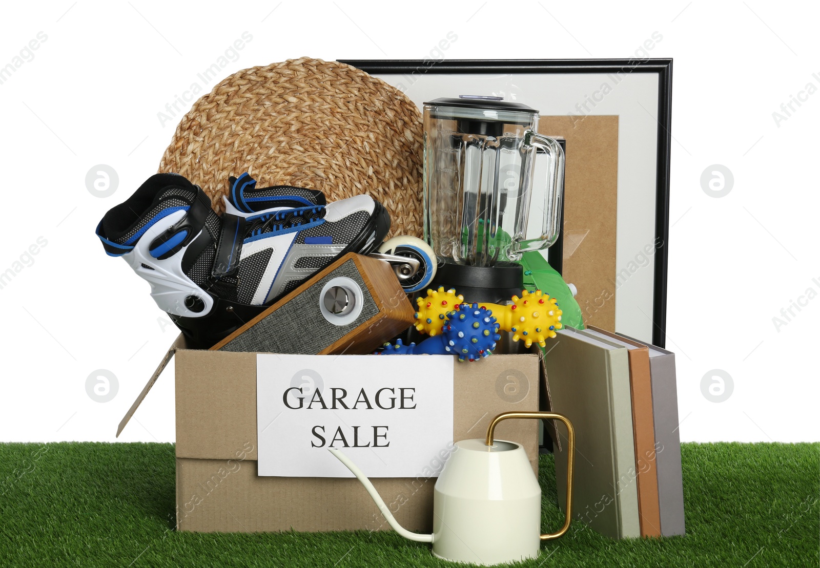 Photo of Box with sign Garage Sale and different stuff on green grass against white background