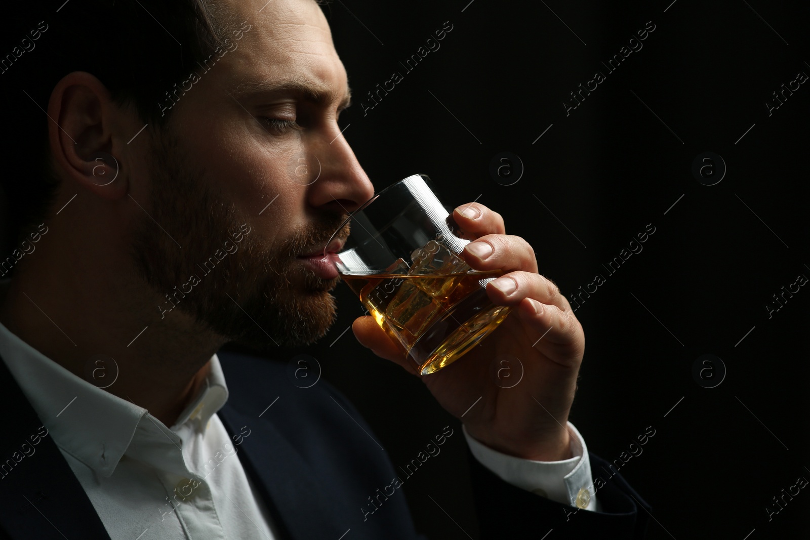 Photo of Man in suit drinking whiskey on black background