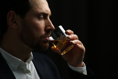 Man in suit drinking whiskey on black background