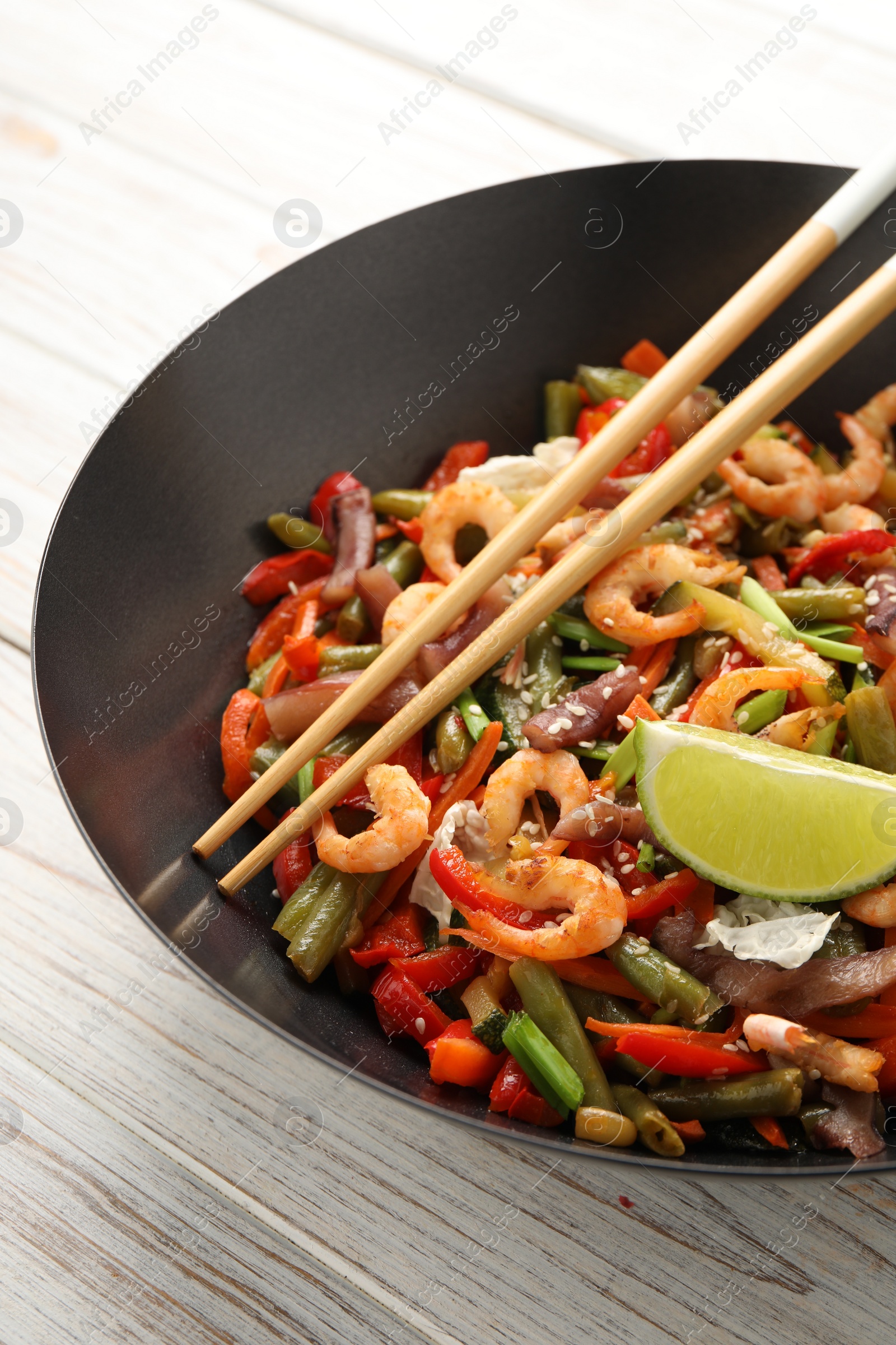 Photo of Shrimp stir fry with vegetables in wok and chopsticks on light wooden table, closeup