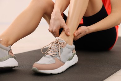 Photo of Woman suffering from leg pain on exercise mat indoors, closeup