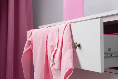 Pink shirt on white chest of drawers indoors, closeup