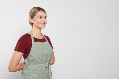 Photo of Beautiful young woman in clean apron on light grey background. Space for text