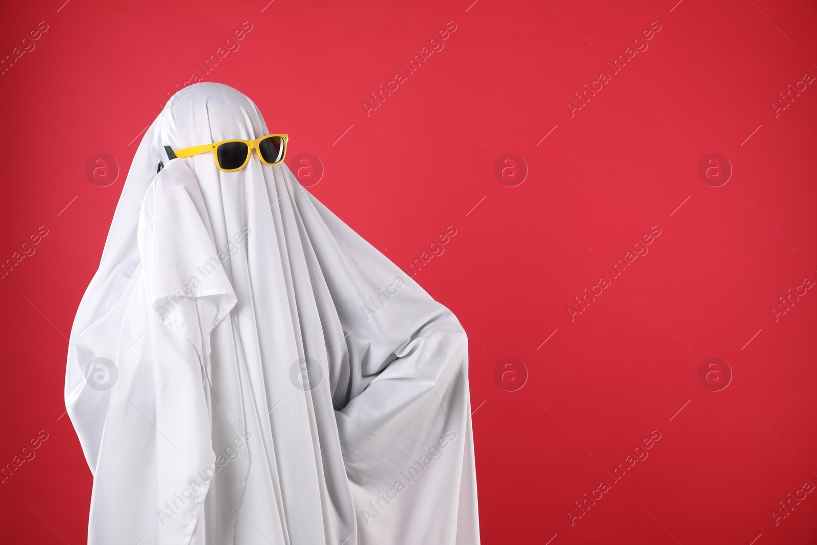 Photo of Person in ghost costume and sunglasses talking on smartphone against red background, space for text