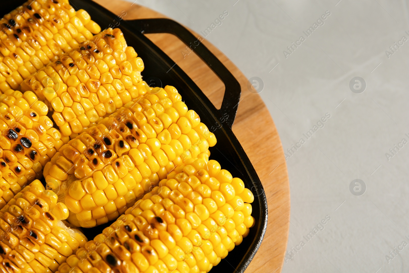 Photo of Fresh grilled tasty corn cobs in pan and space for text on light background