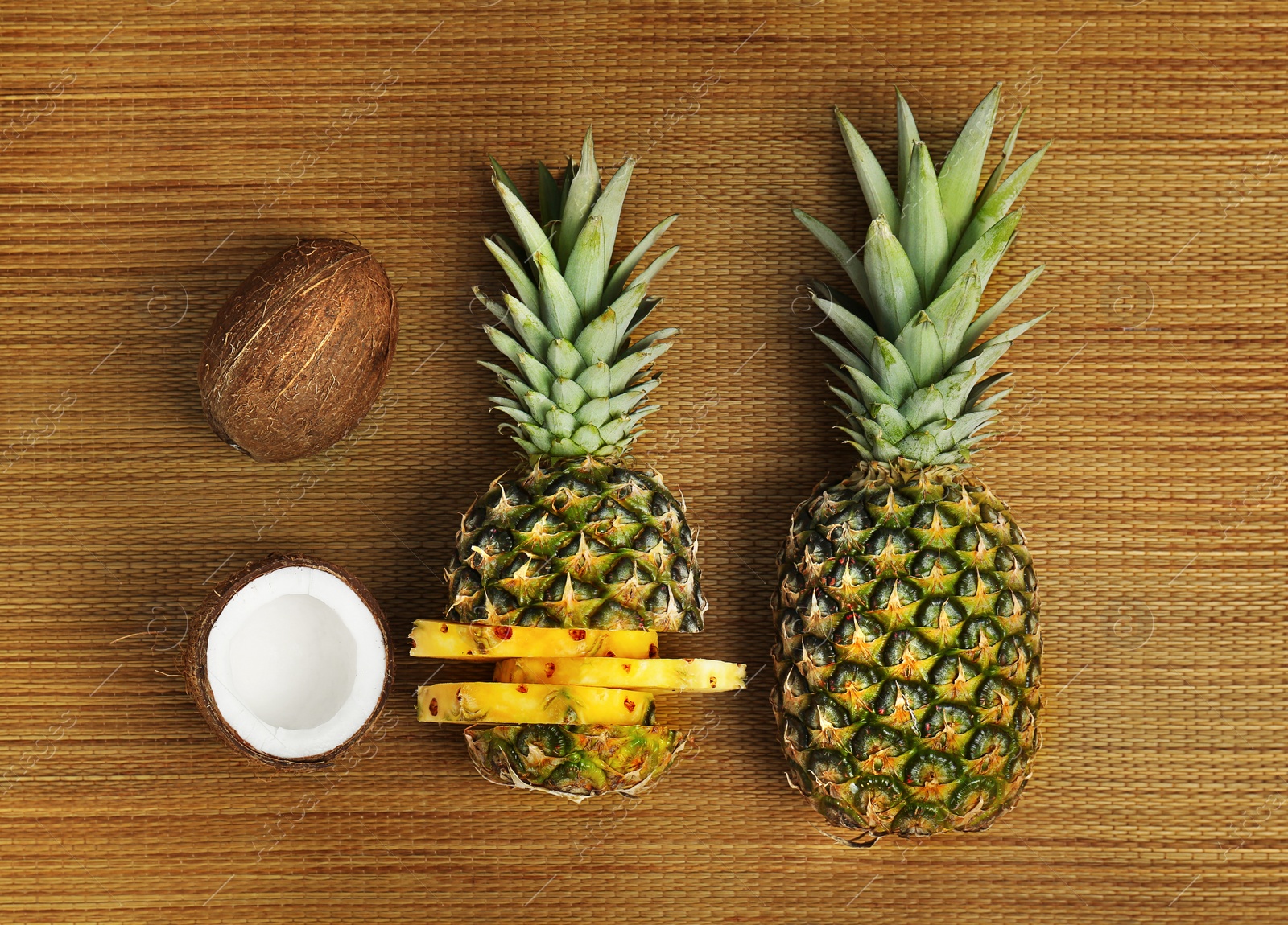 Photo of Fresh pineapples and coconuts on bamboo mat, flat lay