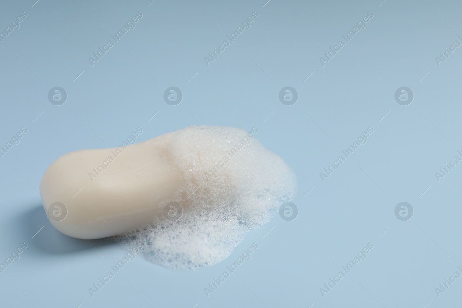 Photo of Soap with fluffy foam on light blue background. Space for text