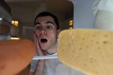 Shocked man near refrigerator in kitchen at night, view from inside