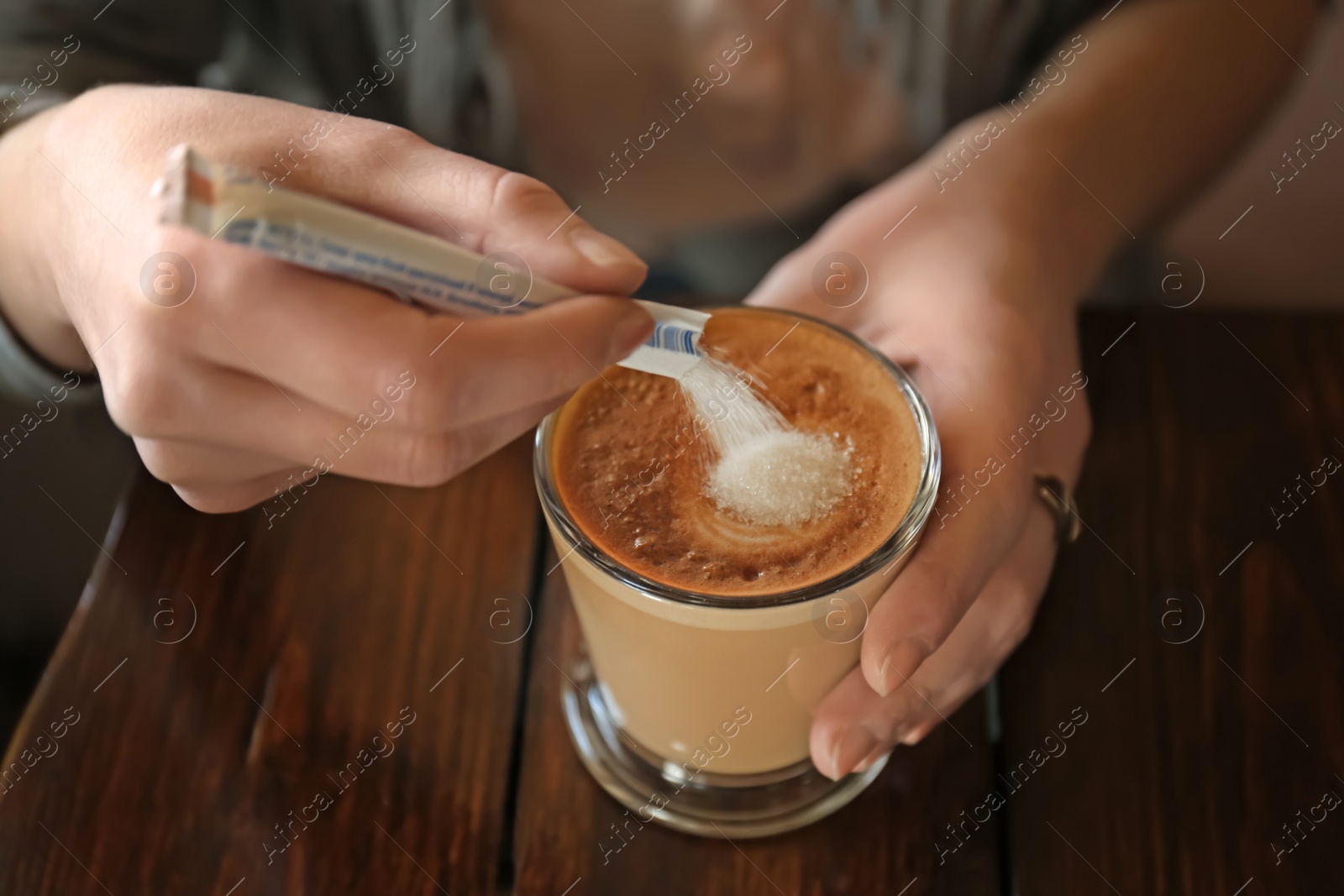 Photo of Woman adding sugar to aromatic coffee at wooden table