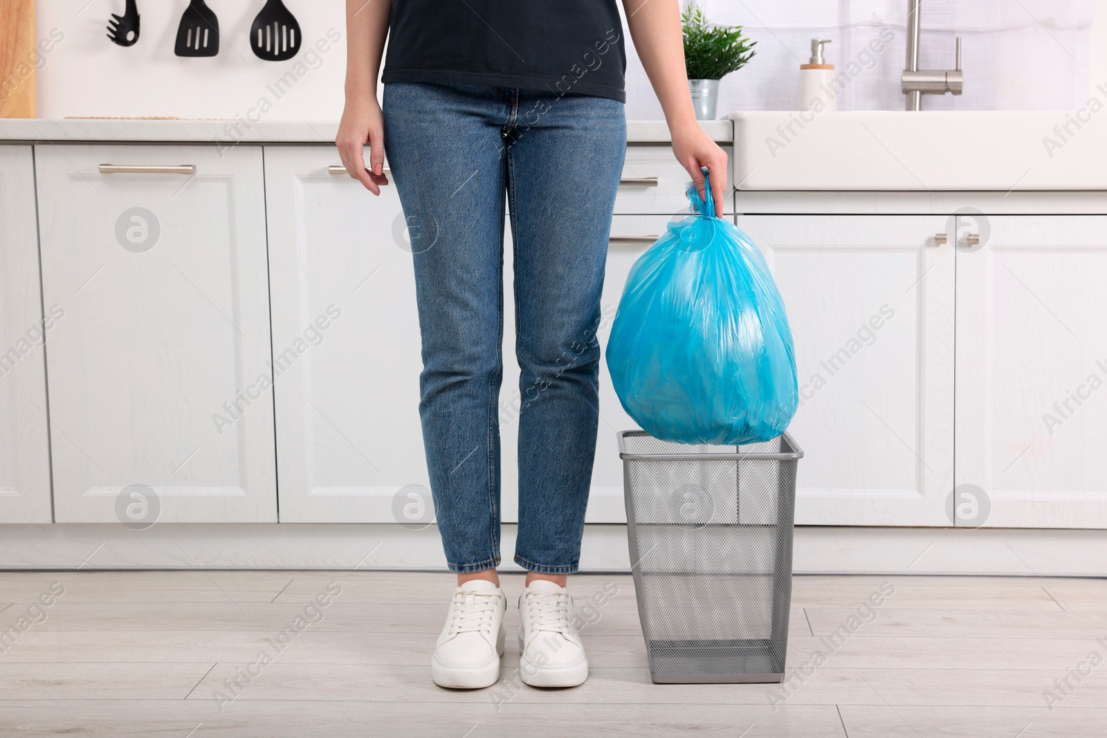 Photo of Woman taking garbage bag out of trash bin in kitchen, closeup