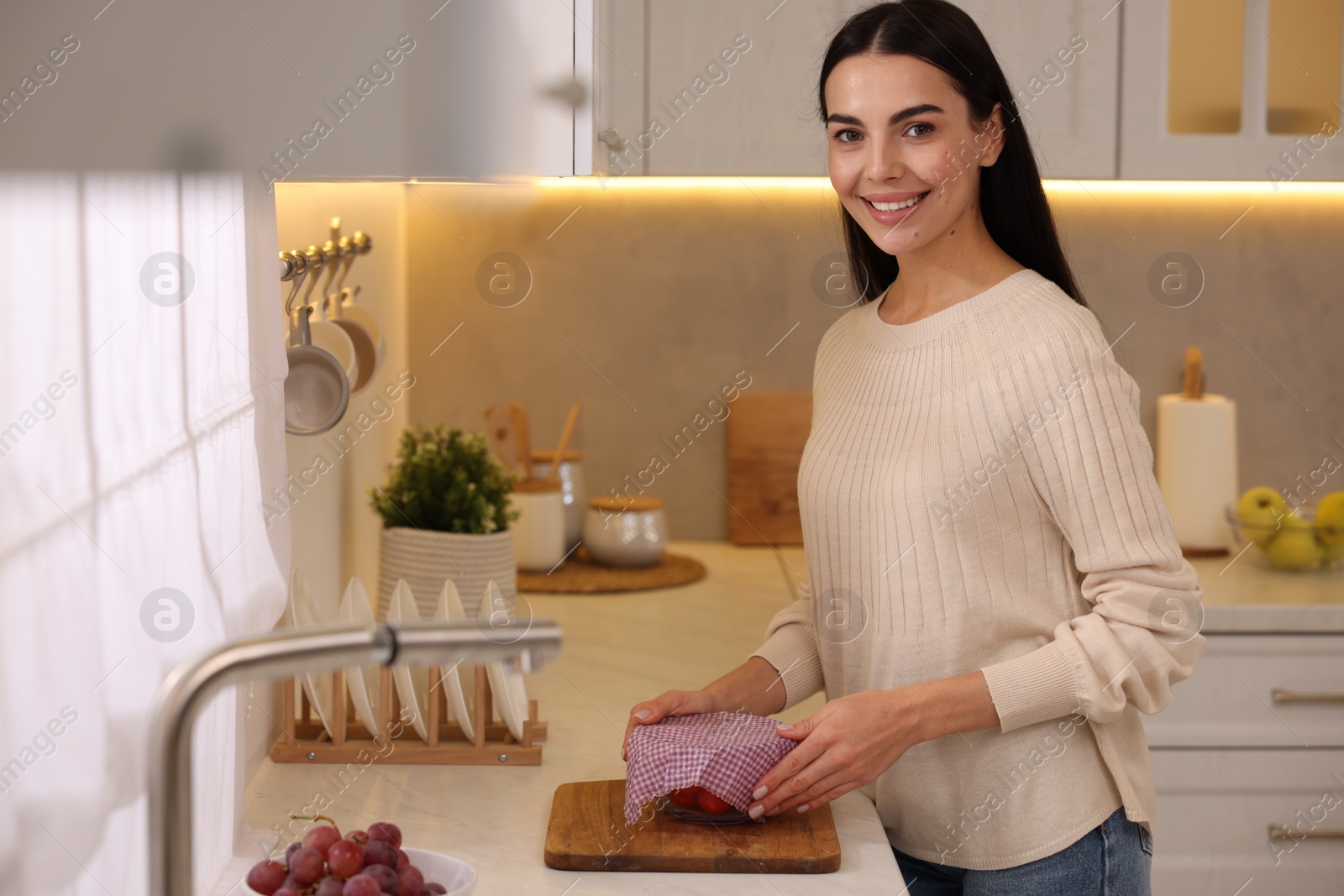 Photo of Happy woman packing bowl into beeswax food wrap at countertop in kitchen