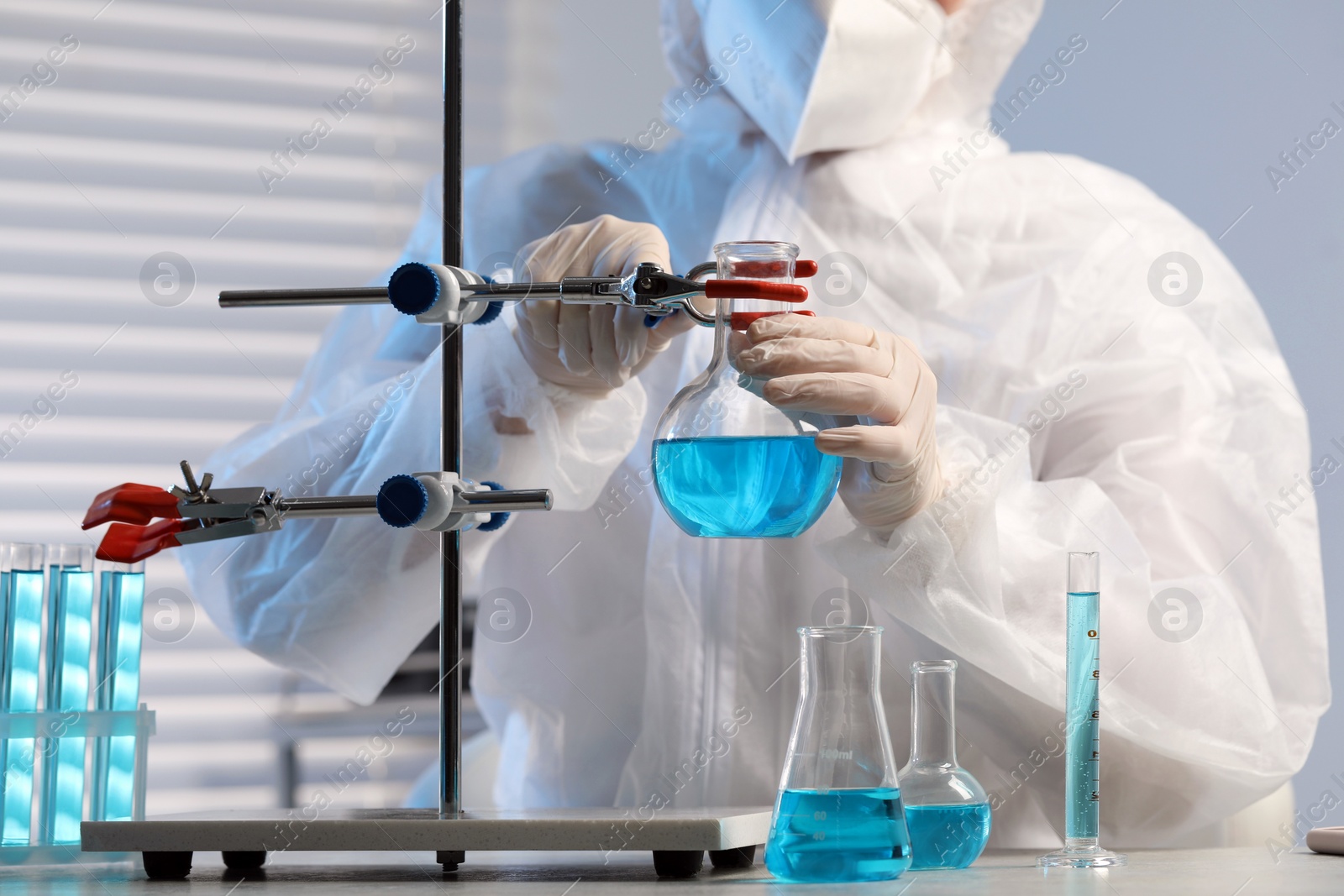 Photo of Scientist working with flask of light blue liquid in laboratory, closeup