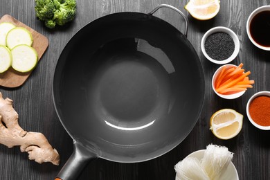 Photo of Empty iron wok surrounded by ingredients on dark grey wooden table, flat lay