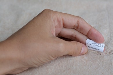 Photo of Woman holding white clothing label on beige garment, closeup