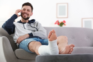 Photo of Man with broken leg in cast using mobile phone while sitting on sofa at home