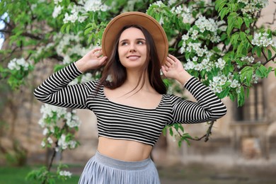 Photo of Beautiful woman in hat near blossoming tree on spring day