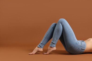 Woman wearing stylish light blue jeans on brown background, closeup. Space for text