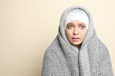 Young woman wrapped in blanket suffering from fever on light background, space for text. Cold symptoms