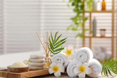 Photo of Composition with different spa products, plumeria flowers and palm leaves on table in bathroom