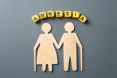 Yellow cubes with word Amnesia and figure of senior couple on grey background, top view