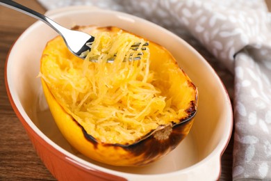 Photo of Half of cooked spaghetti squash and fork in baking dish on table, closeup