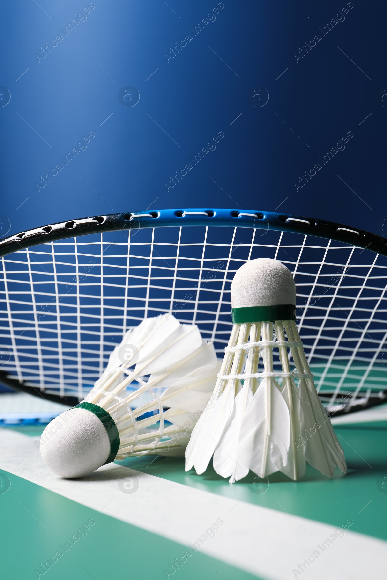 Photo of Feather badminton shuttlecocks and racket on green table against blue background, closeup