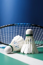 Photo of Feather badminton shuttlecocks and racket on green table against blue background, closeup