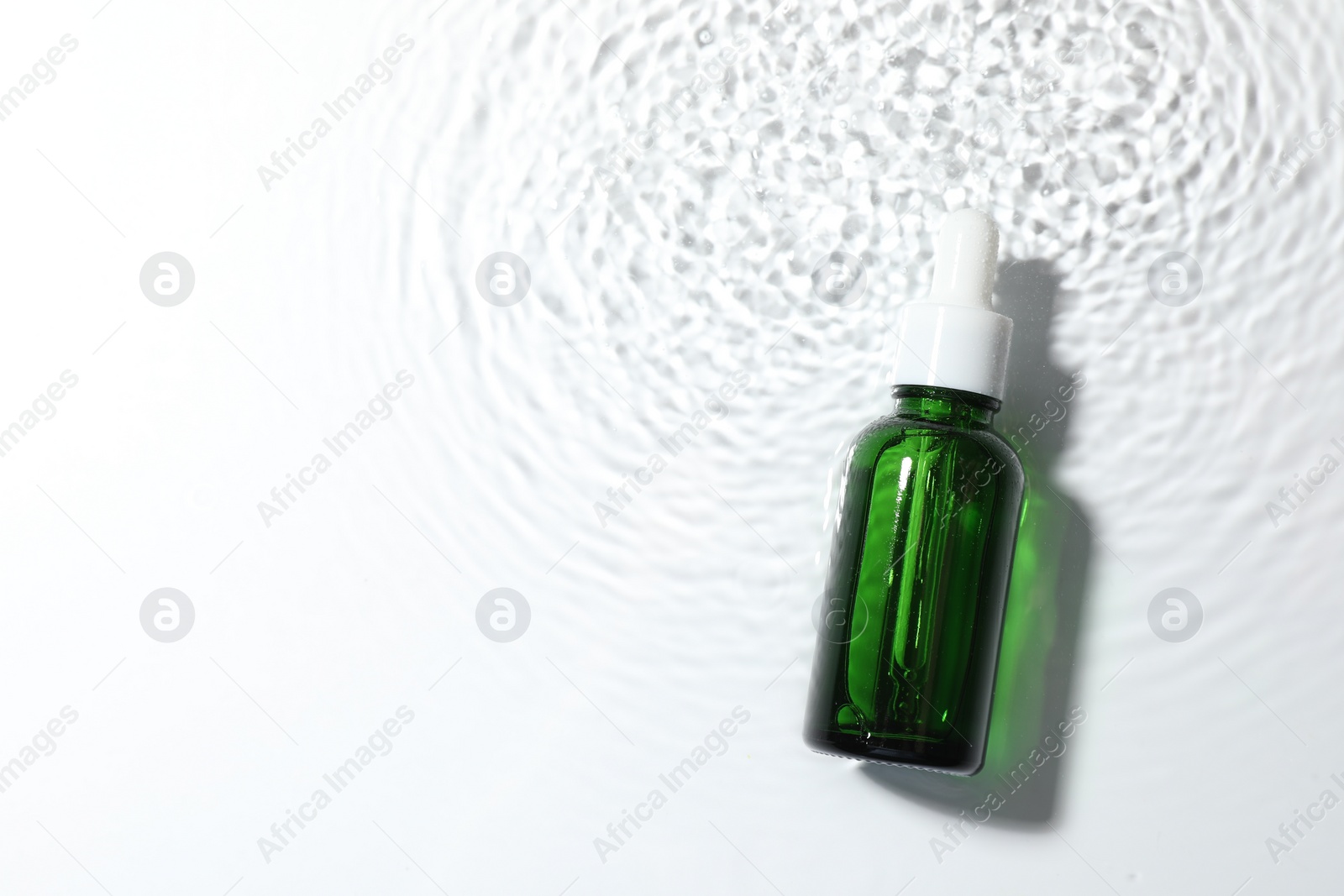 Photo of Bottle of cosmetic product in water on white background, top view. Space for text