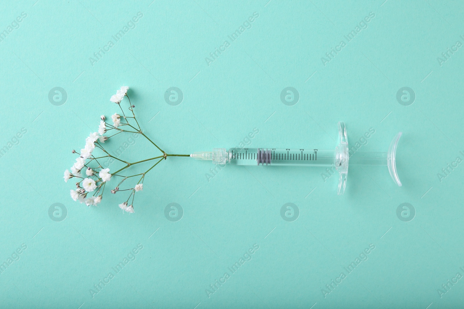 Photo of Cosmetology. Medical syringe and gypsophila on turquoise background, top view