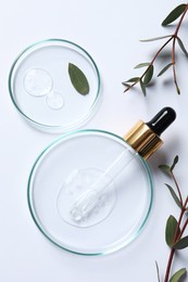 Petri dishes with samples of cosmetic oil, pipette and green leaves on white background, flat lay