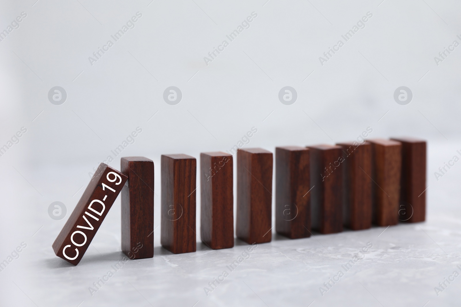 Photo of Falling wooden domino tiles on grey marble table. Spreading of coronavirus concept