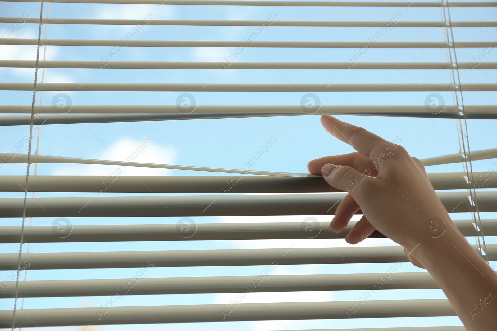 Photo of Woman opening horizontal window blinds at home, closeup. Space for text